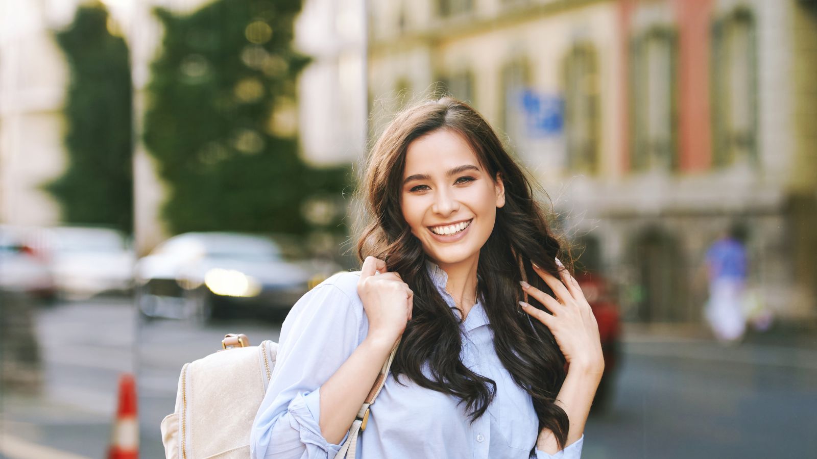 A photo of a happy traveler walking through a charming European street carrying a small suitcase and backpack.