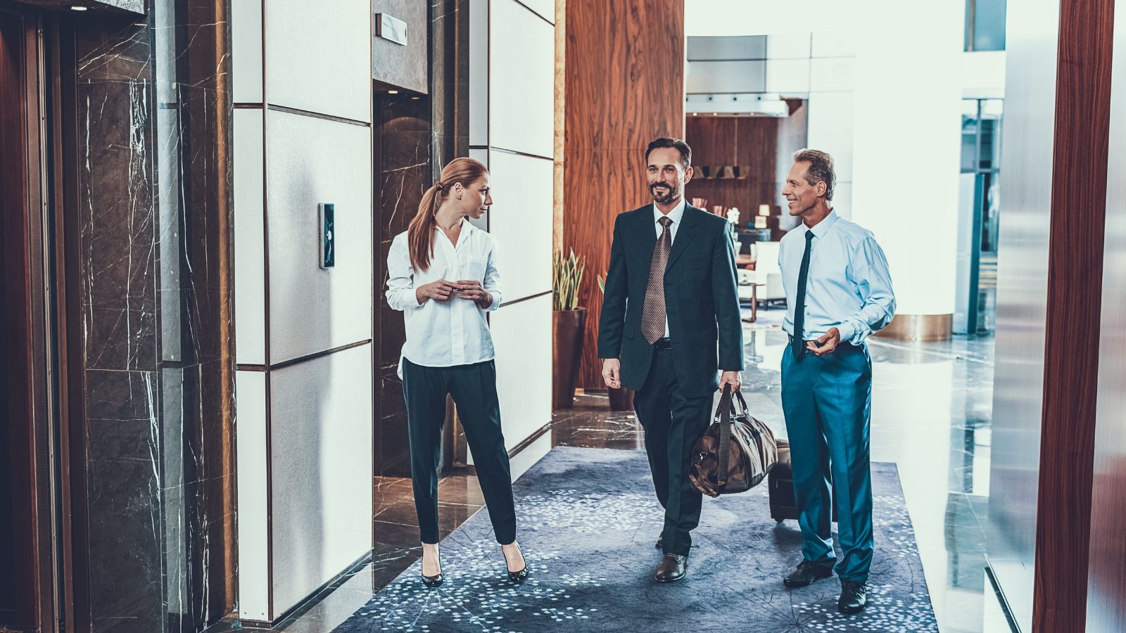 A photo of hotel hallway with elevator and guest rooms, traveler looking thoughtful while considering room location.