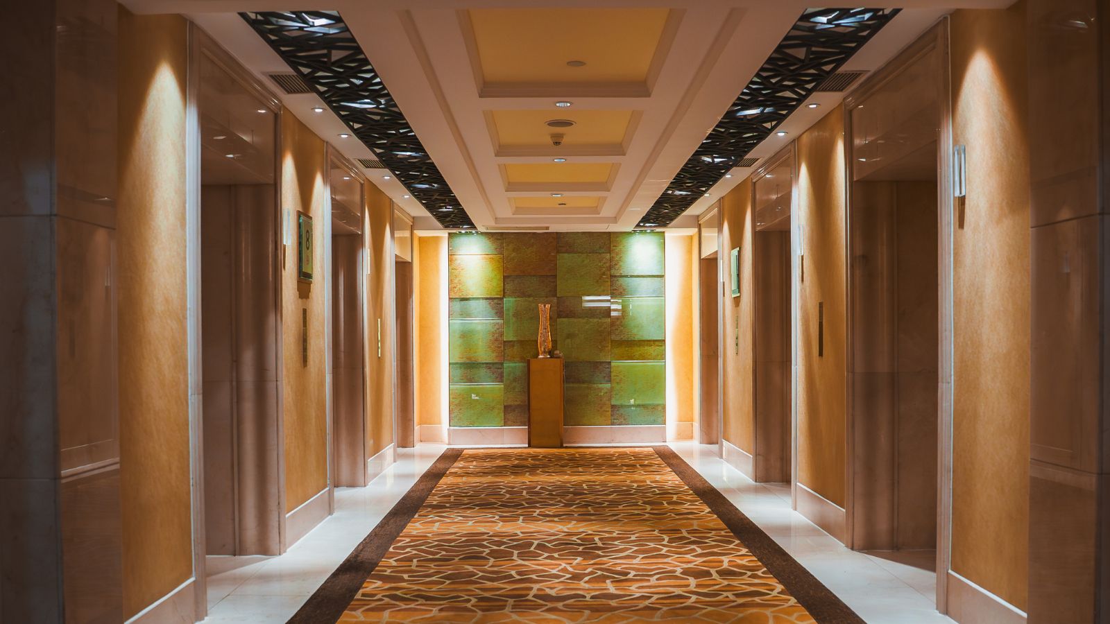 A photo of modern hotel room beside elevator with illuminated floor indicator and hallway traffic.