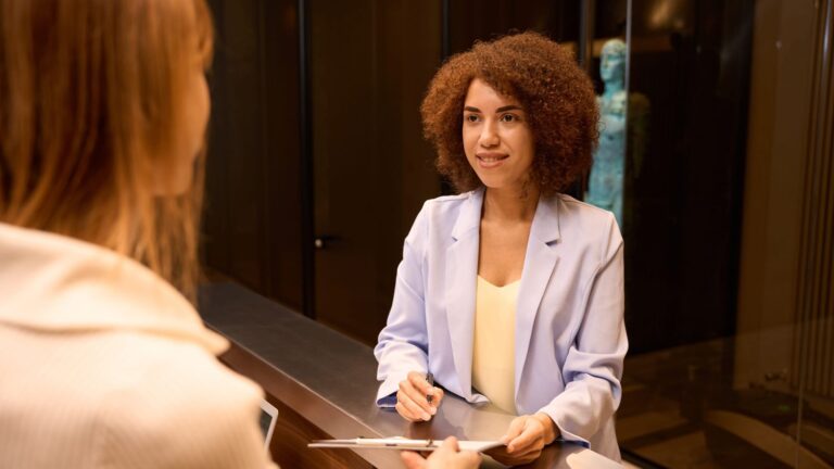 A photo of a “hotel guest checking in at front desk speaking with receptionist polite interaction modern hotel lobby candid.