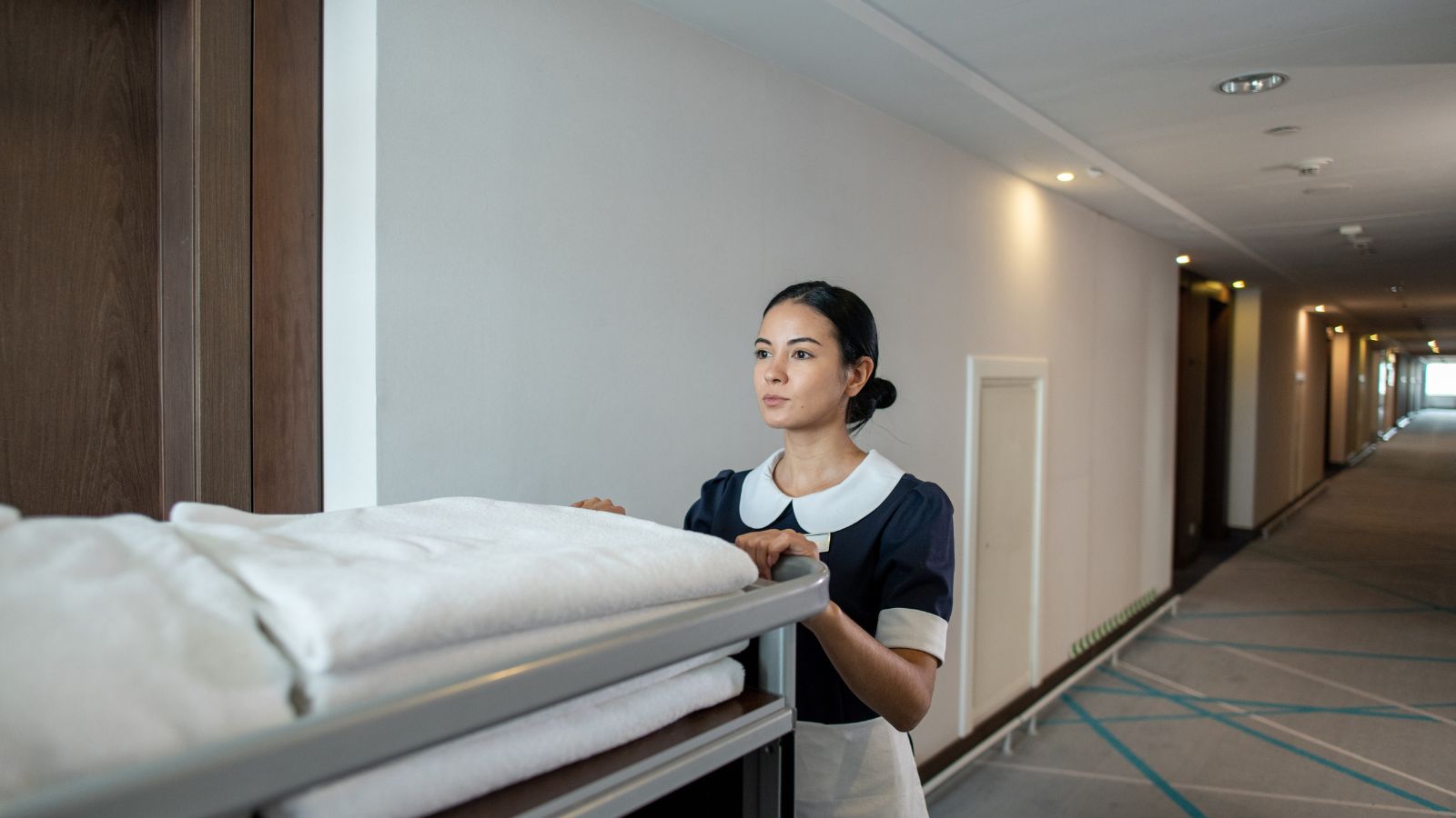 A photo of hotel hallway with elevator and housekeeping cart outside guest room door.