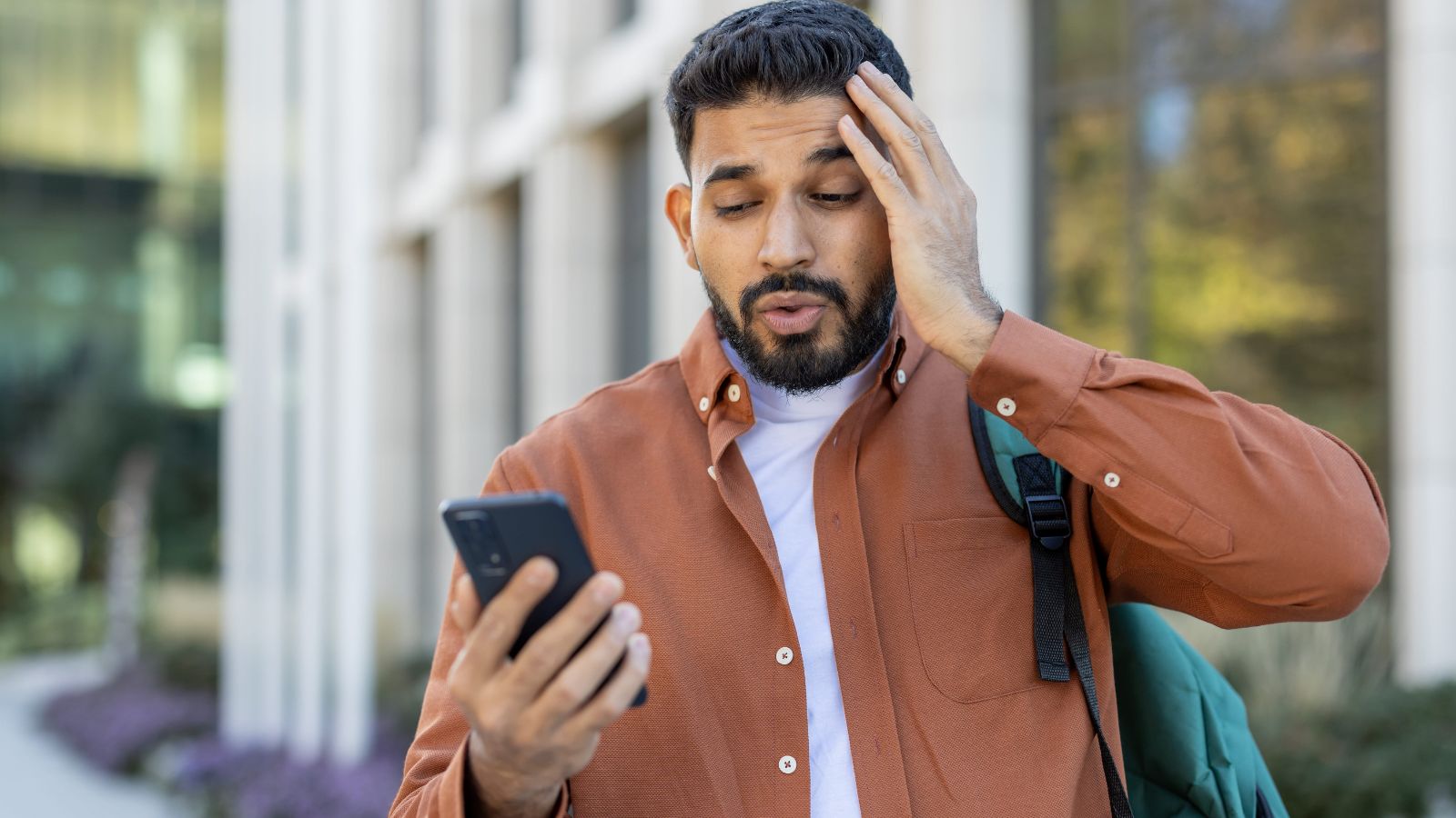 A photo of a man that looks puzzled and stress looking at his phone.