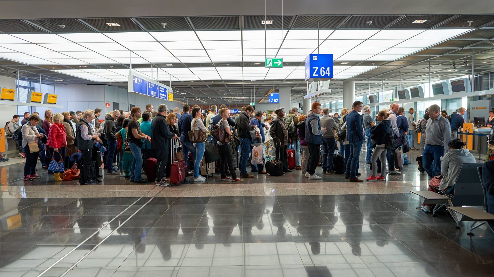 Travelers with luggage wait in line at a brightly lit airport check-in area.