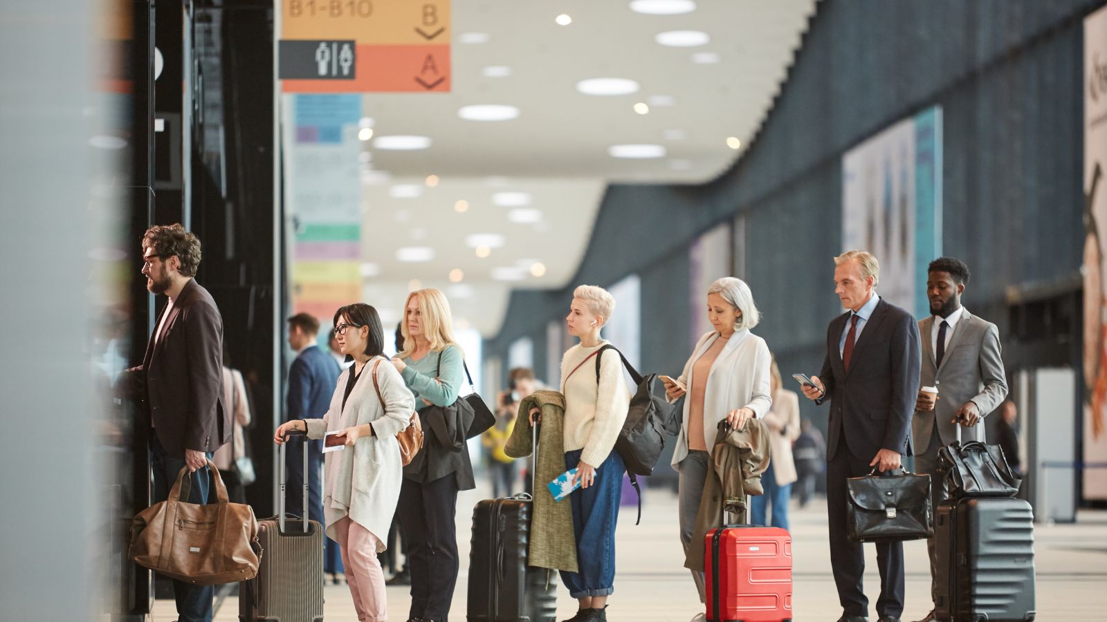 People with suitcases line up at an airport terminal near a departure gate.
