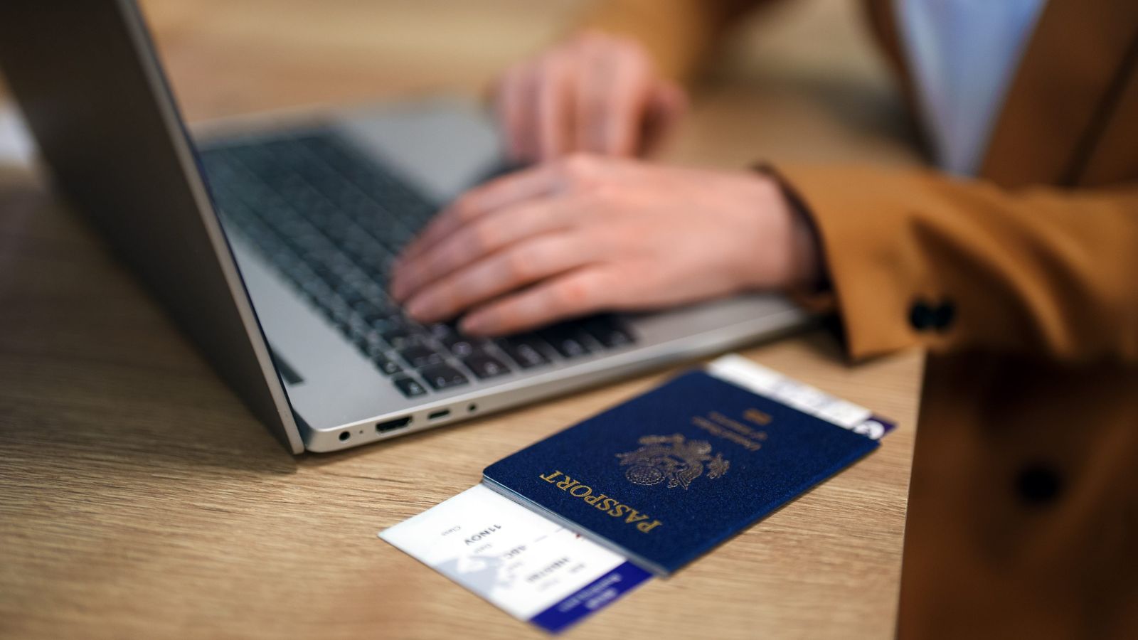 A photo of a traveler reviewing flight details and total travel costs on a laptop with passport and boarding pass nearby.