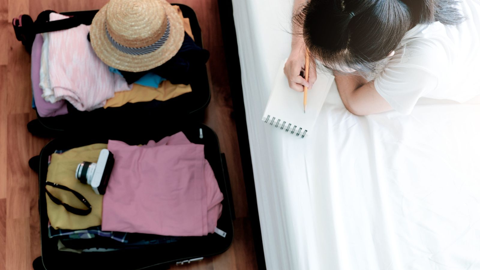 A photo that describes a traveler sitting on bed planning outfits with open suitcase many clothes considering what to pack natural candid.