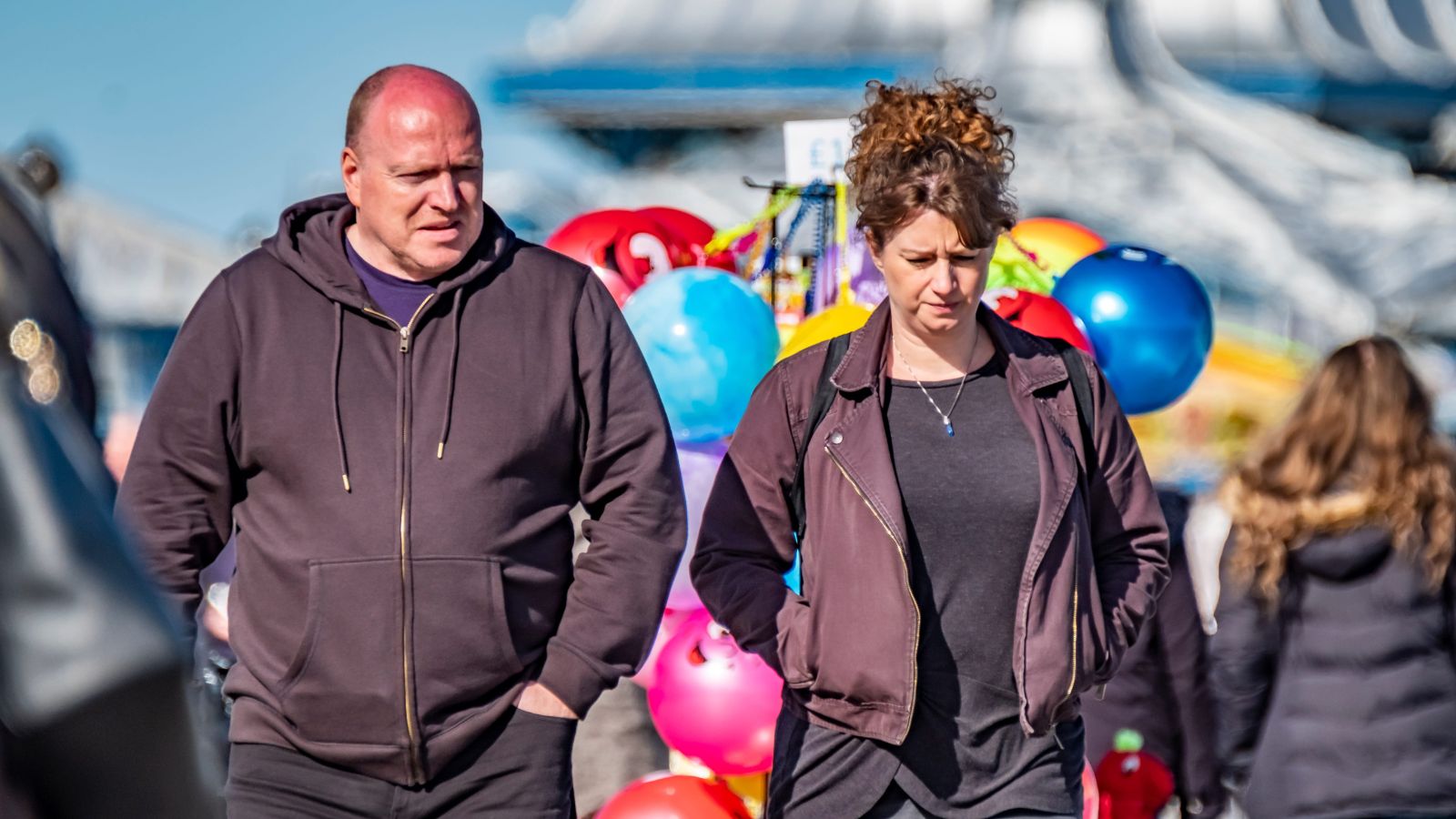 A photo of mature couple walking fast through crowded tourist area looking tired and rushed holding map or phone busy sightseeing schedule travel fatigue candid natural light.