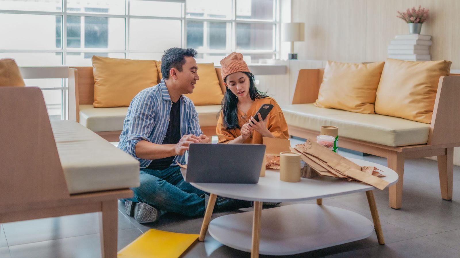 A photo of couple sitting at the floor facing laptop.