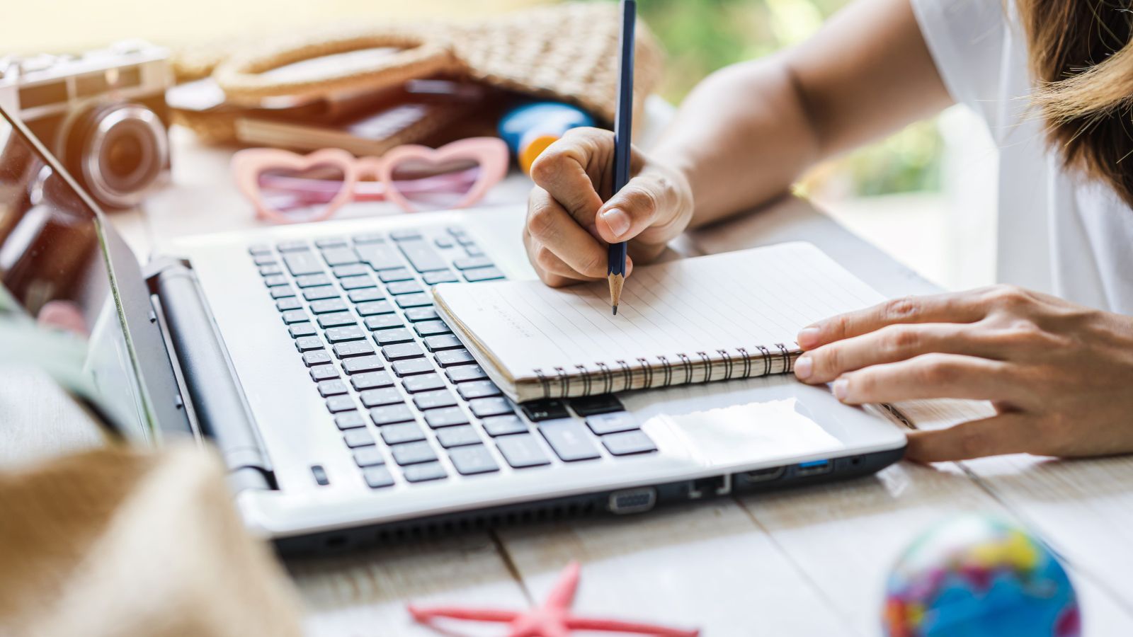 A picture that shows a woman facing a laptop, with a notebook and a pen.