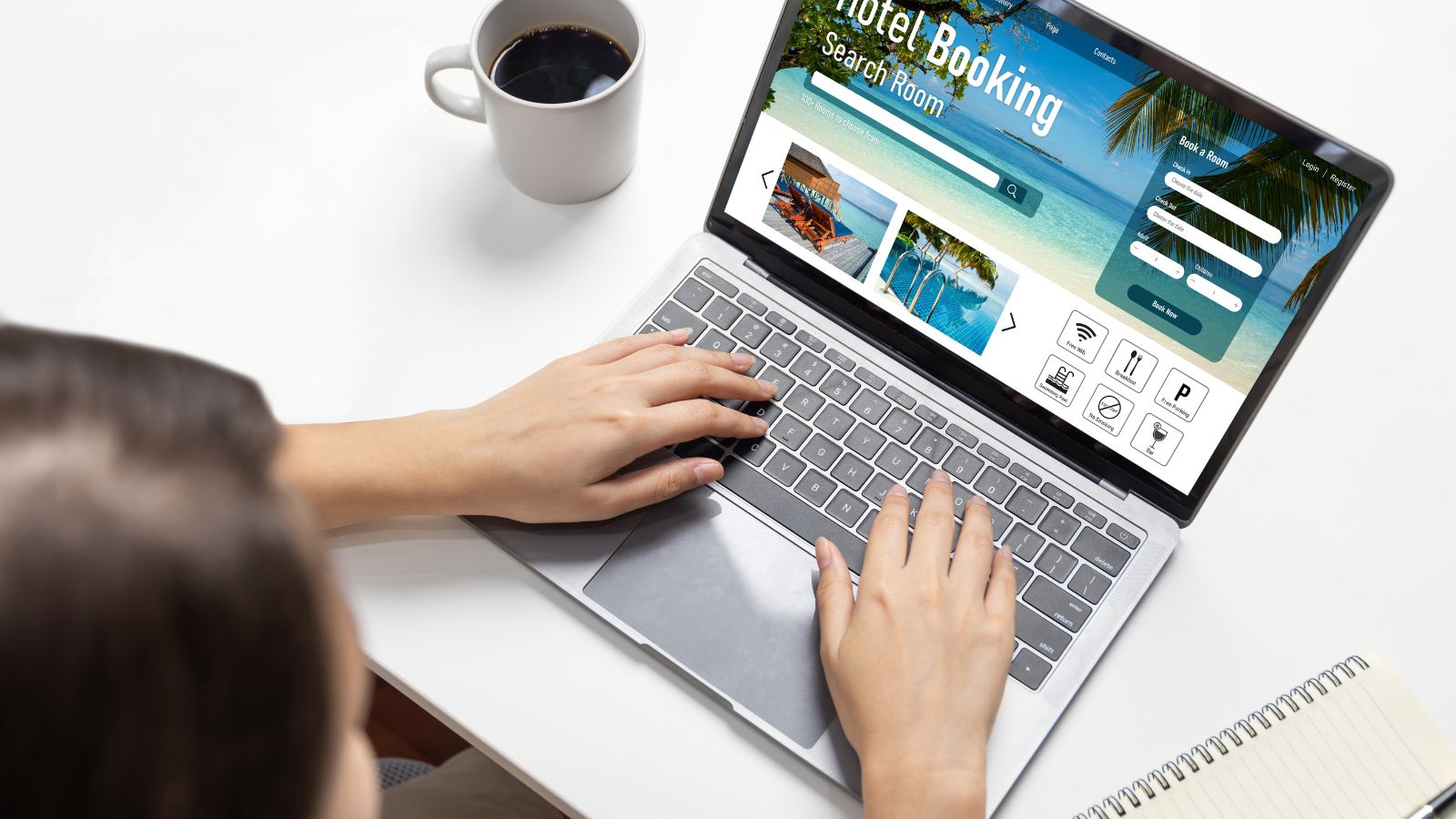 A photo of traveler booking a hotel room on a laptop while sitting at a desk with passport and travel notes nearby