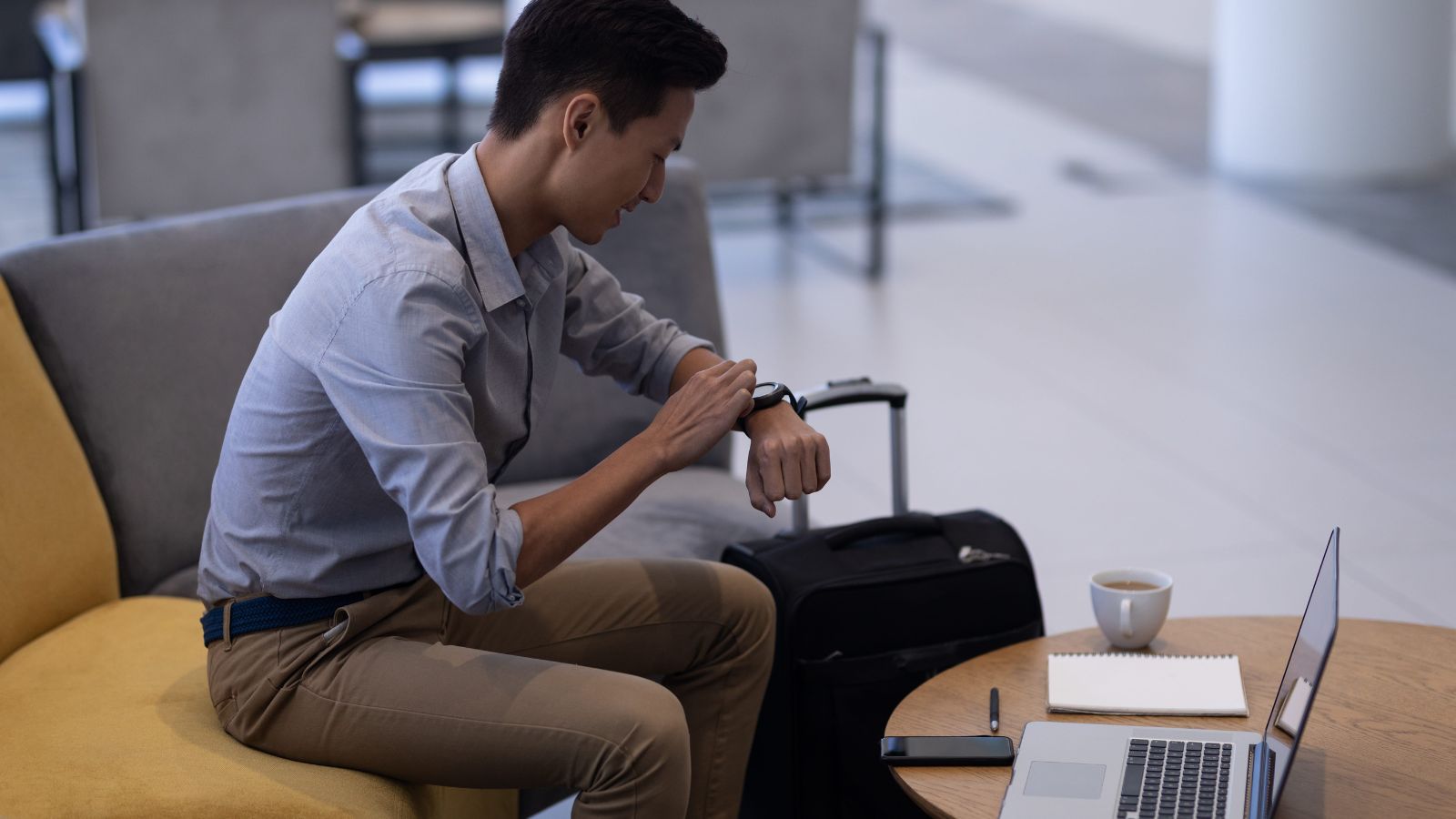 A photo of a tired traveler sitting in hotel lobby with luggage waiting for check in exhausted travel candid realistic.