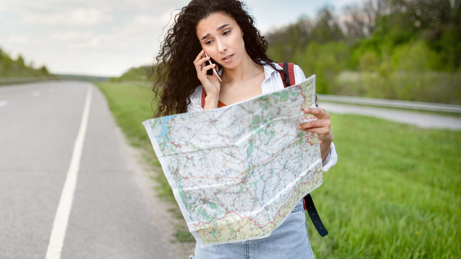 A photo of a woman holding a map while talking to someone at the phone.