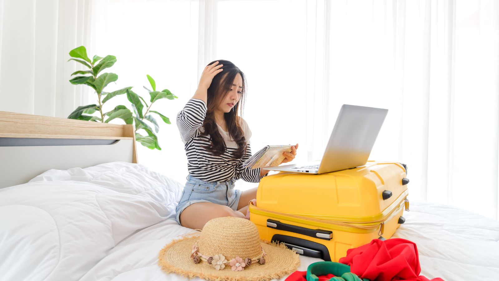 A photo of a woman, sitting in the bed scratching her head looking at her laptop.