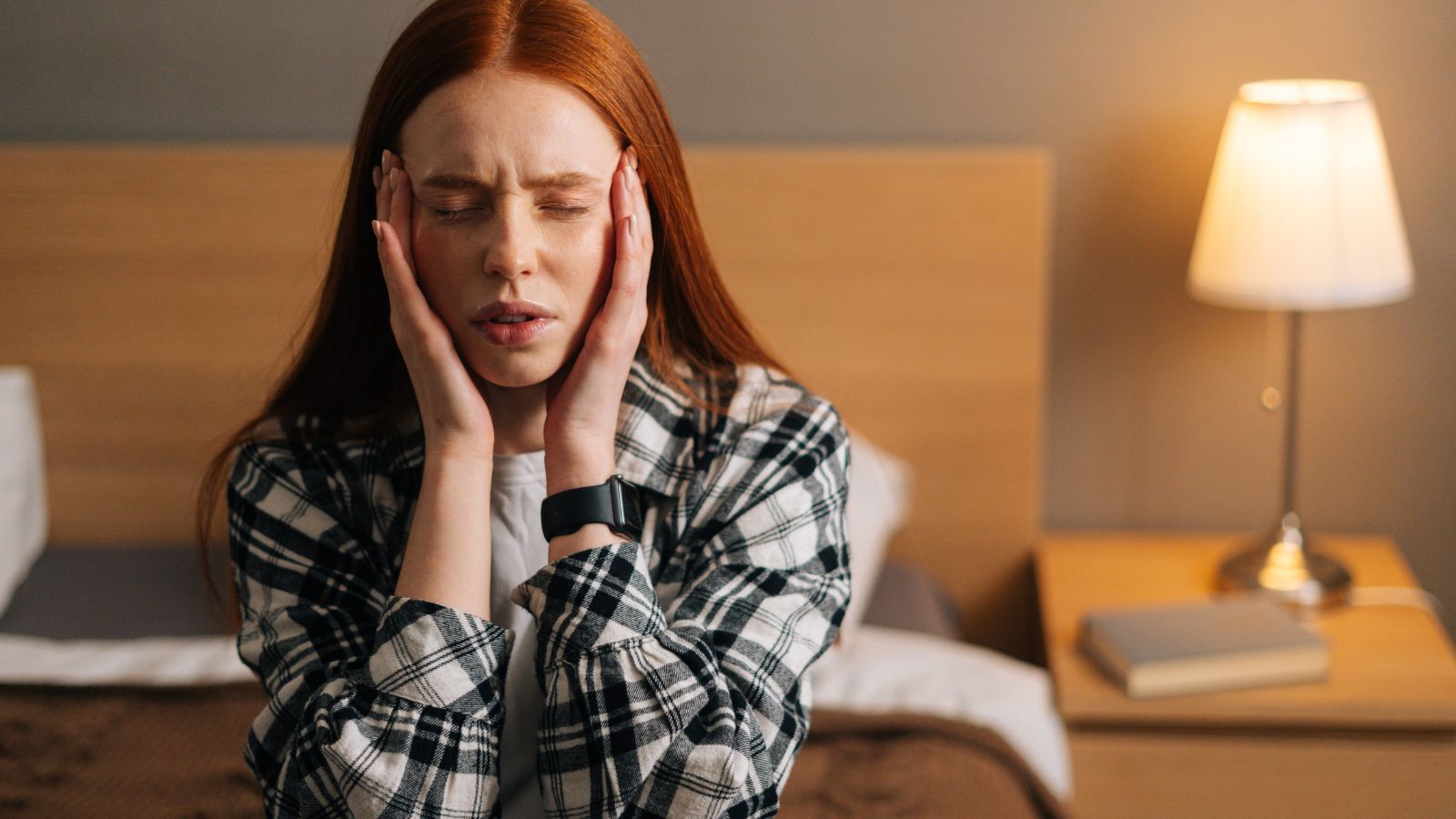 A photo of a traveler sitting in hotel room looking uncomfortable annoyed reacting to noise or poor conditions dim lighting cluttered interior.